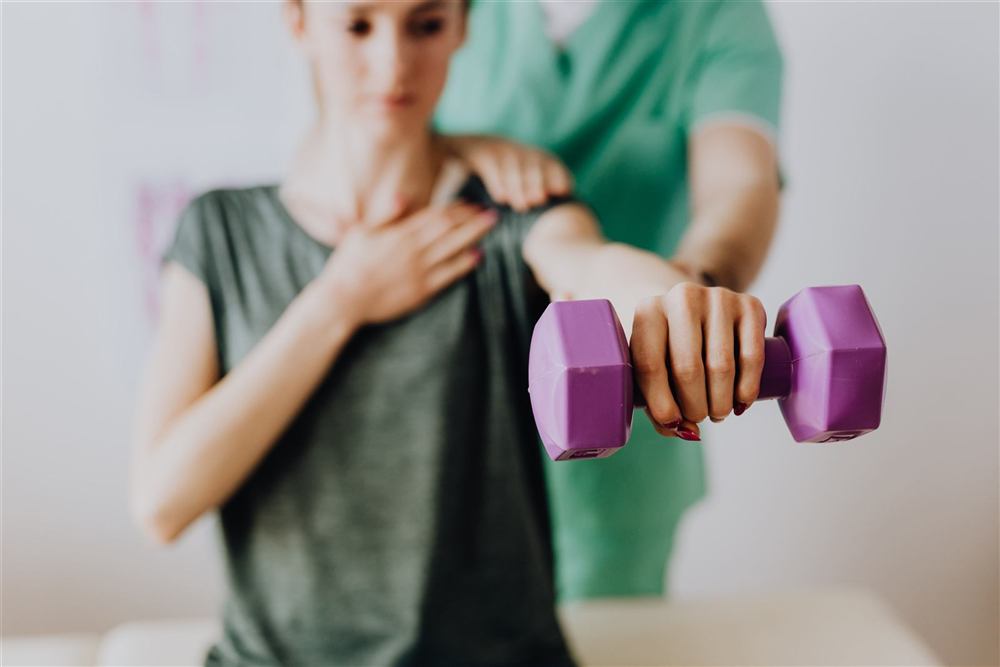Physiotherapist guiding a patient through a shoulder strengthening exercise with a dumbbell